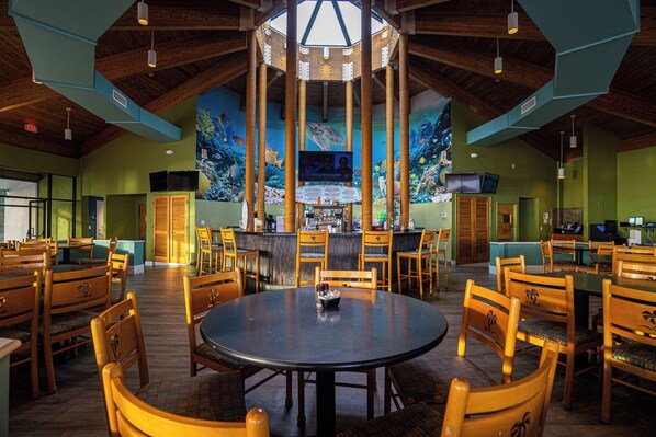 Un restaurant avec des tables et des chaises en bois, un coin bar et une fresque murale représentant une scène sous-marine.