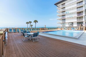 A wooden deck with a pool, outdoor seating, and a view of the beach.