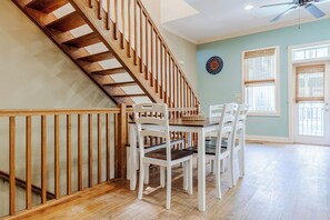 Un comedor con escalera de madera, sillas blancas y una mesa.