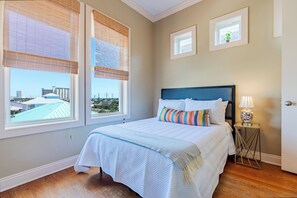 A bedroom with a bed, a nightstand, a lamp, and two windows with blinds. - SeaEsta Luxe Retreat | Pool, Walk to Beach | Activity Opportunities (Panama City Beach)
