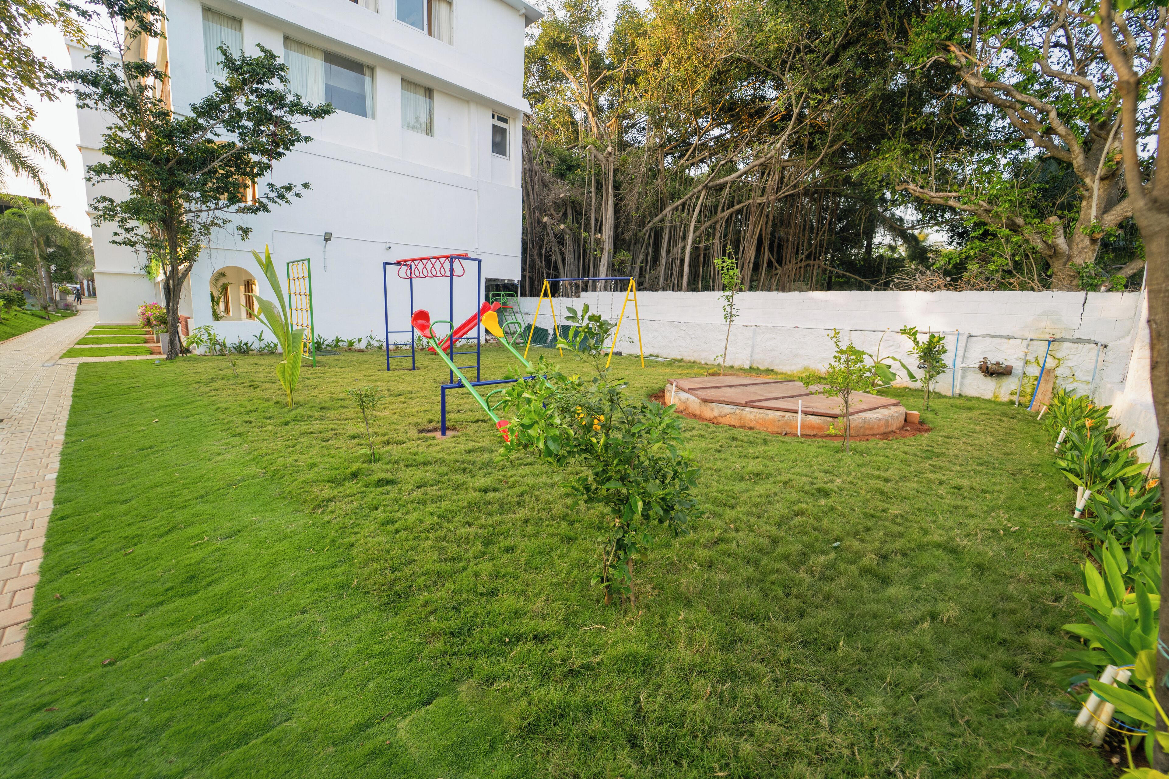 A well-maintained grassy area with a playground, a brick pathway, and a white building with windows.