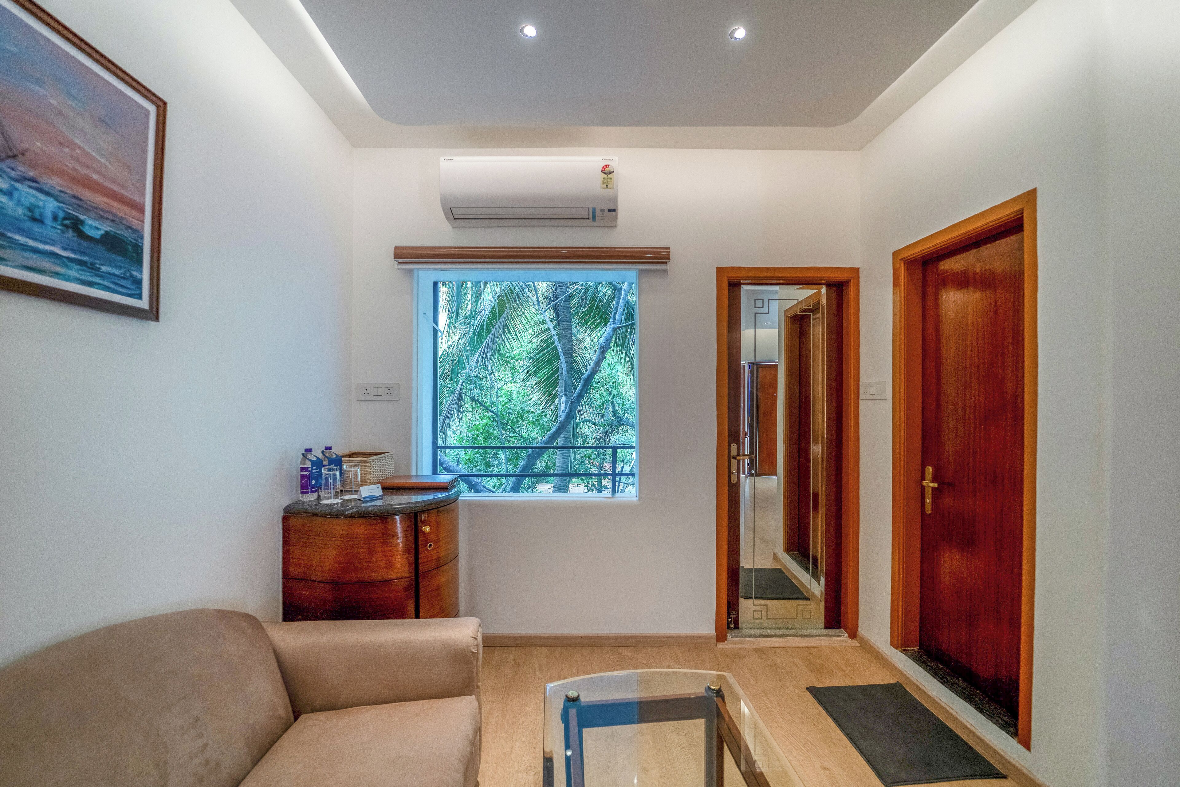 A room with a sofa, a small table, a window with a view of trees, and a door.