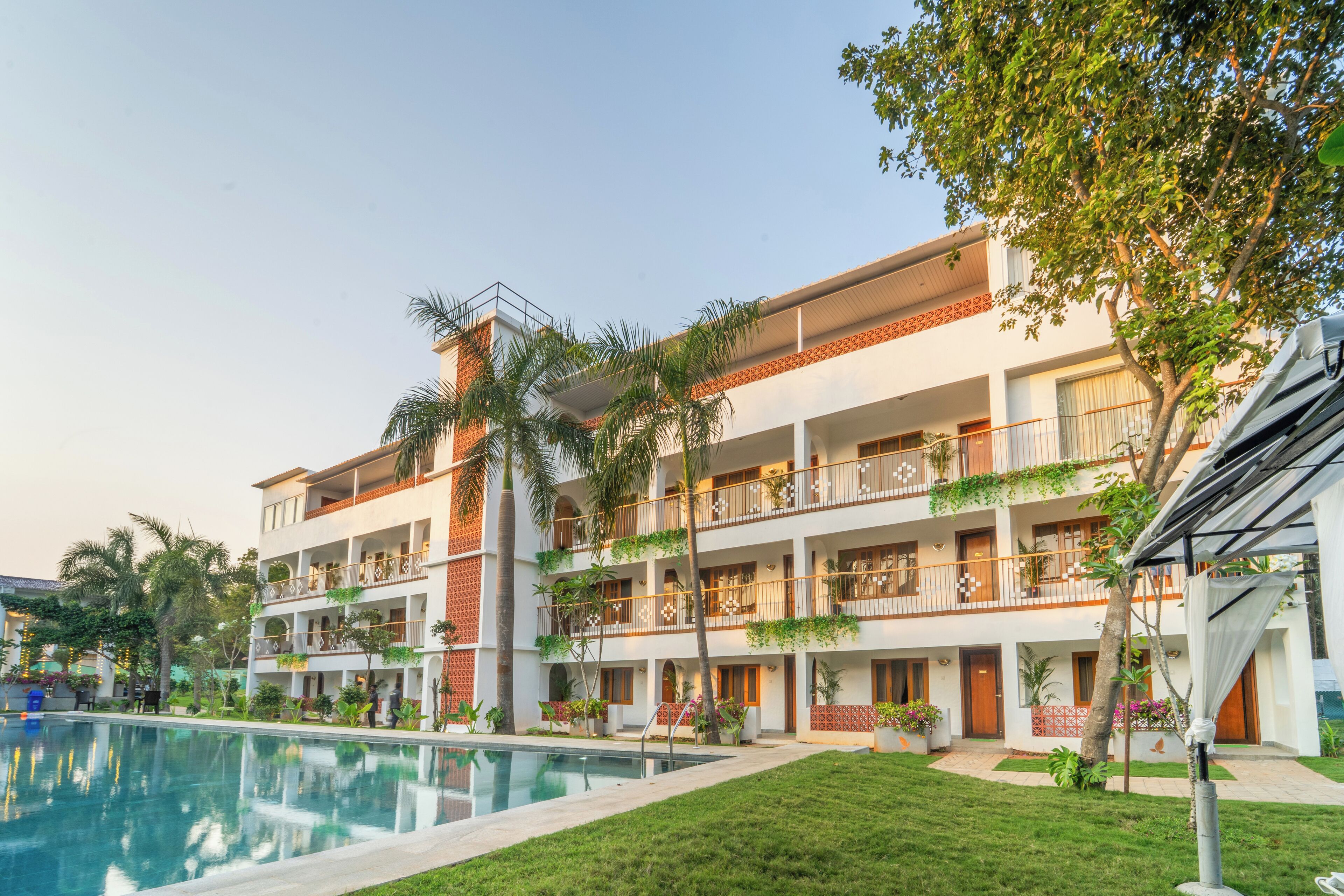 Un hôtel à plusieurs étages doté d’une piscine, de balcons ornés de plantes et d’une pelouse bien entretenue.