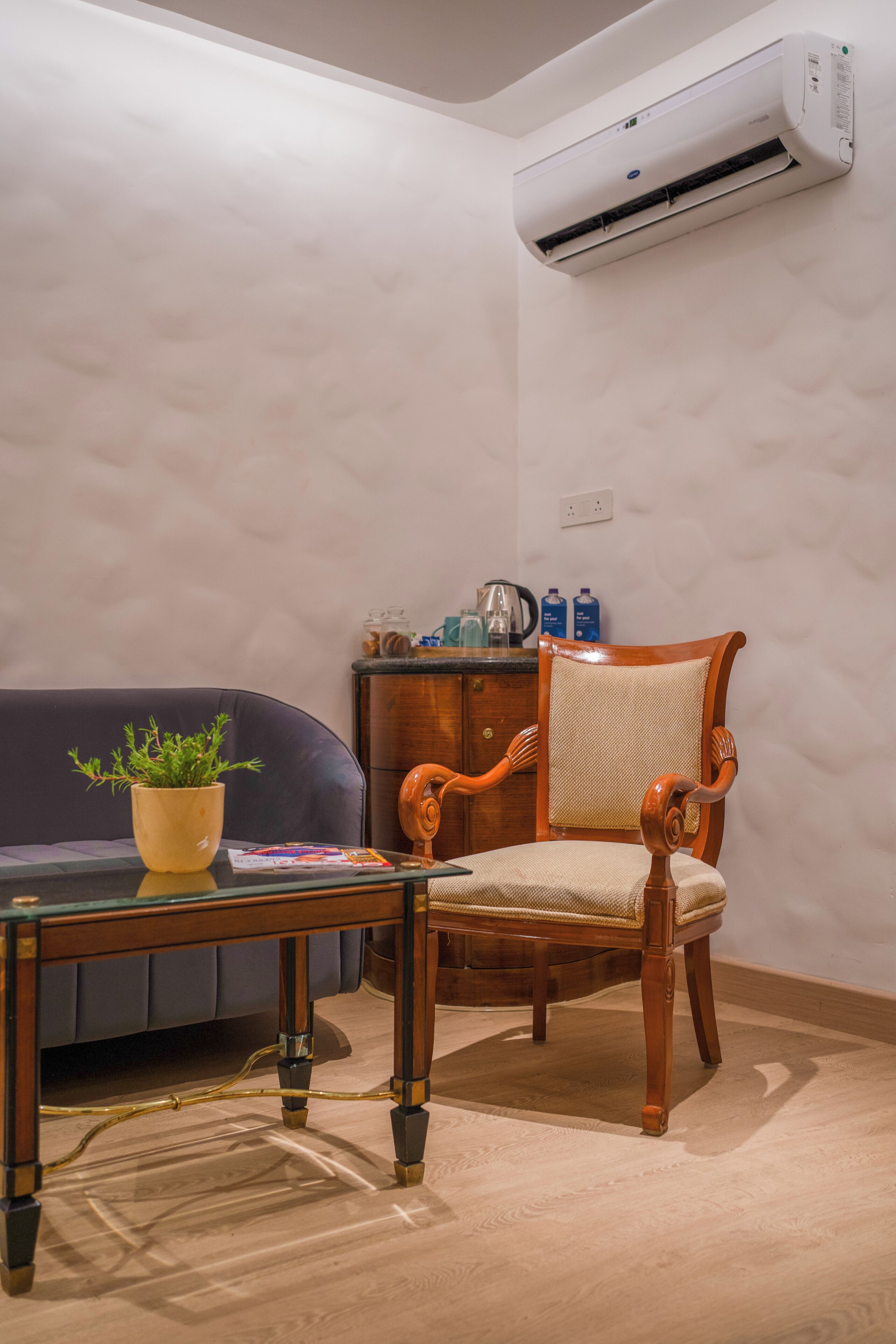 A room with a wooden chair, a glass table, a potted plant, a sofa, and an air conditioning unit.