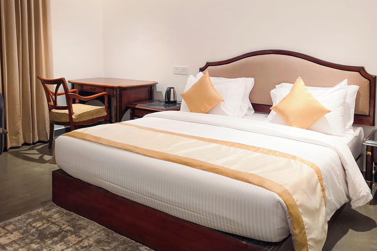 Habitación de hotel con una cama grande, una mesita de noche de madera, una silla y un escritorio.