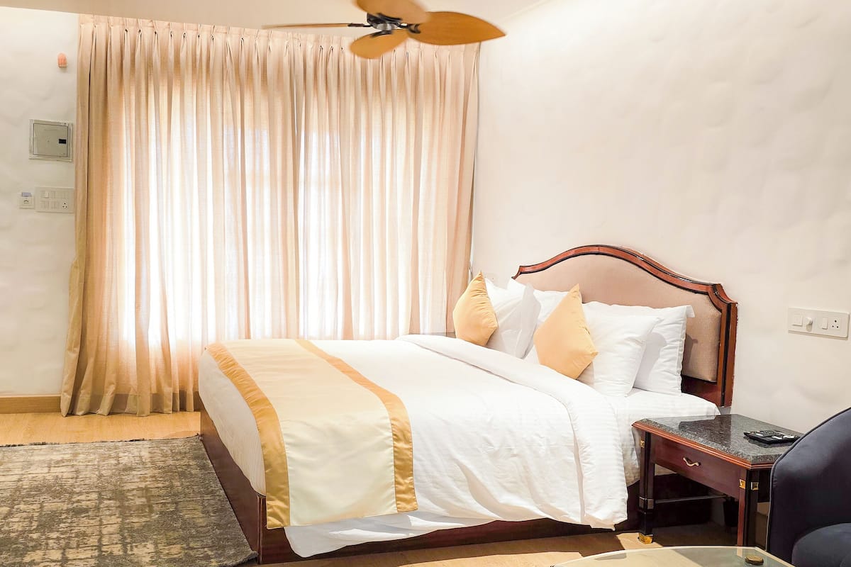 Una habitación de hotel con una cama, un escritorio, una silla, un ventilador de techo y una ventana con cortinas.