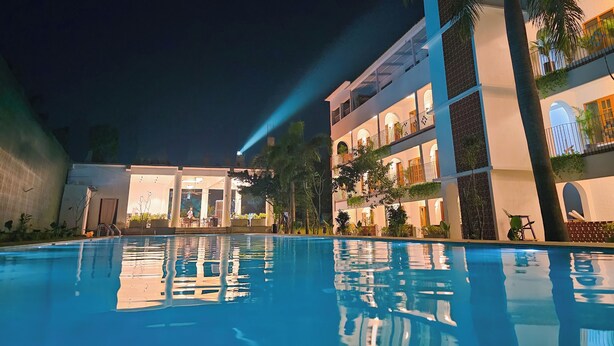 Vista nocturna de un hotel con piscina, varios balcones e iluminación exterior.