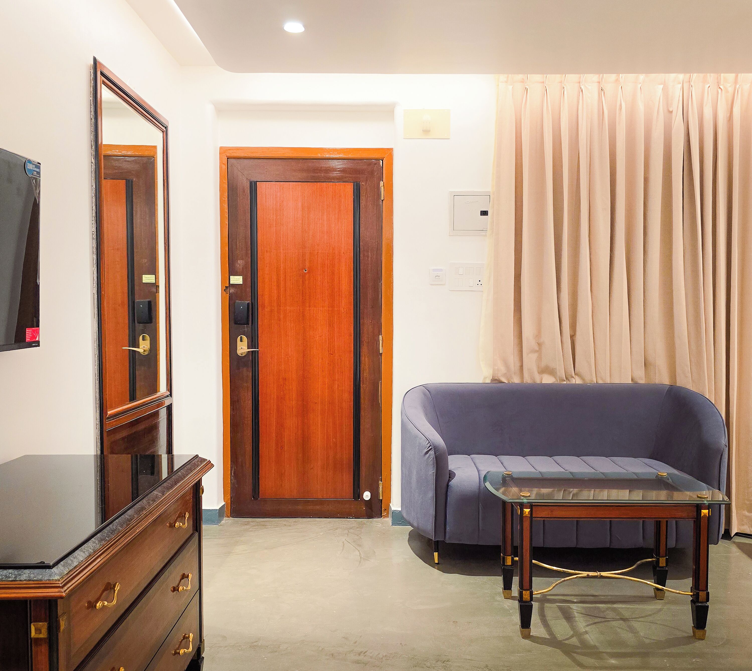A room with a wooden door, a blue sofa, a glass-top table, and a dresser with drawers.