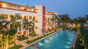 Un hotel con piscina, varios balcones y exuberante jardinería.