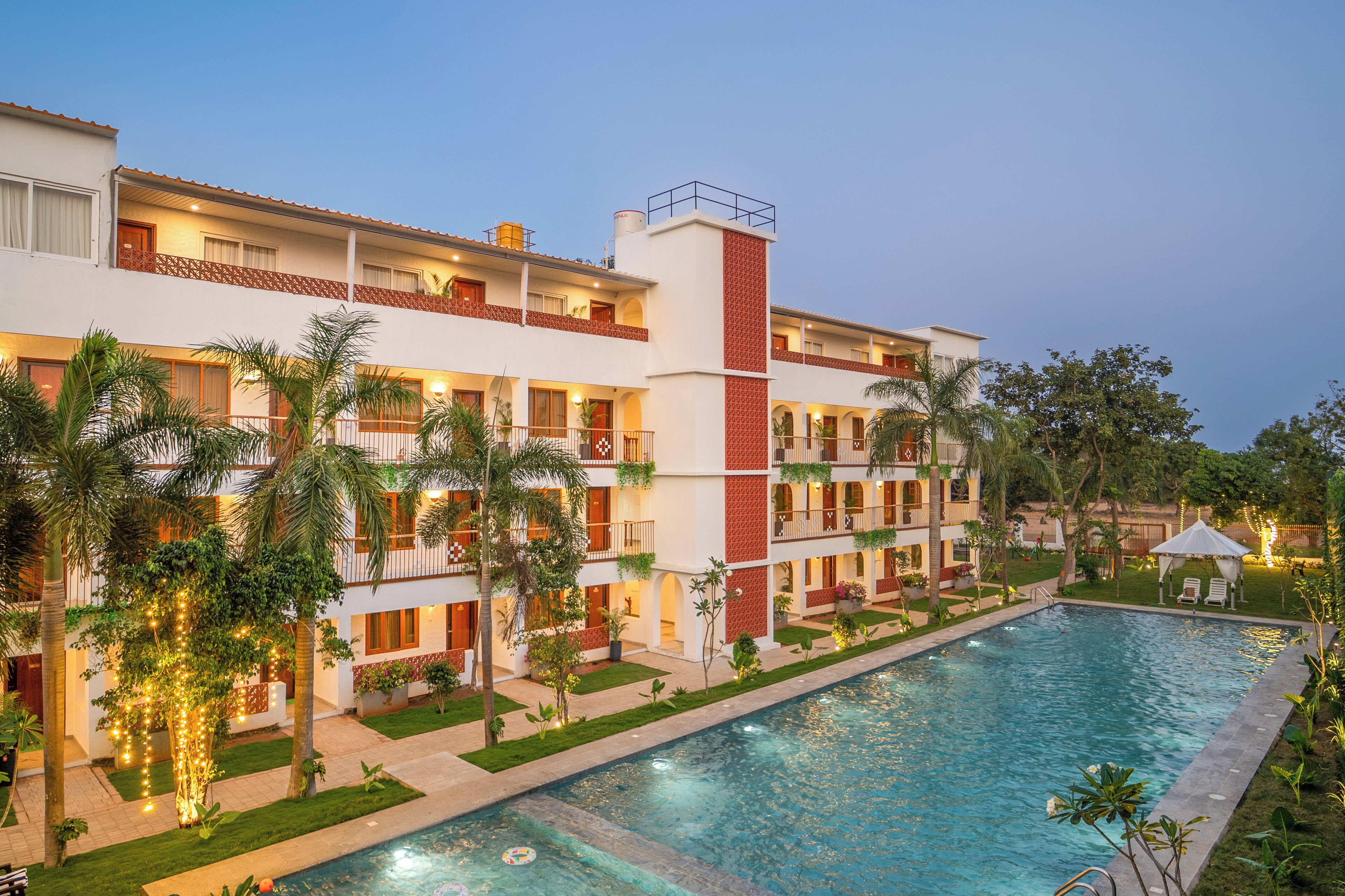 A hotel with a swimming pool, multiple balconies, and palm trees.