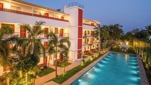 Un hotel con piscina, varios balcones y abundante vegetación.