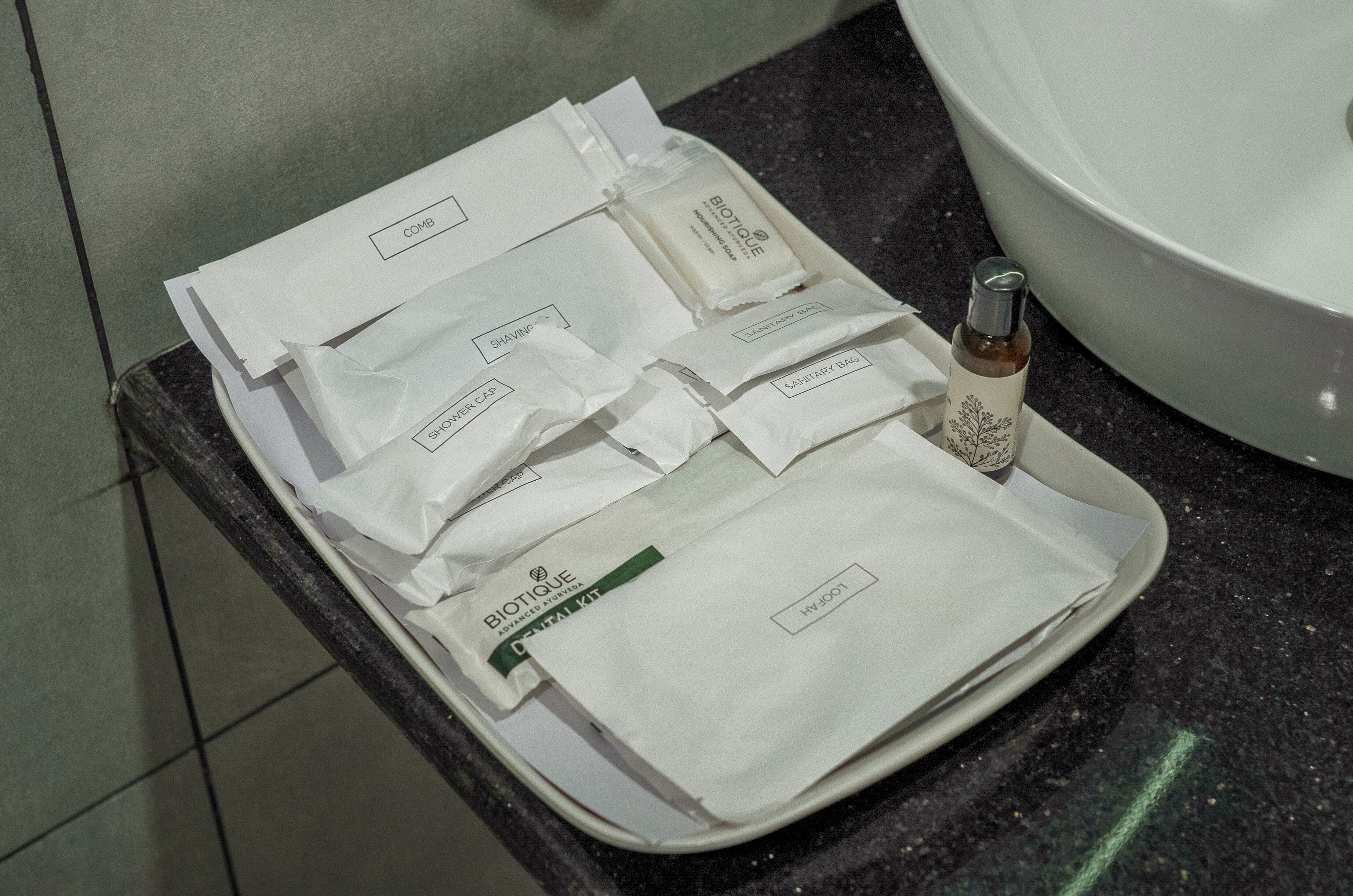 A tray with various toiletries including shaving cream, a bottle of hand sanitizer, and a facial mist, placed on a countertop near a sink.
