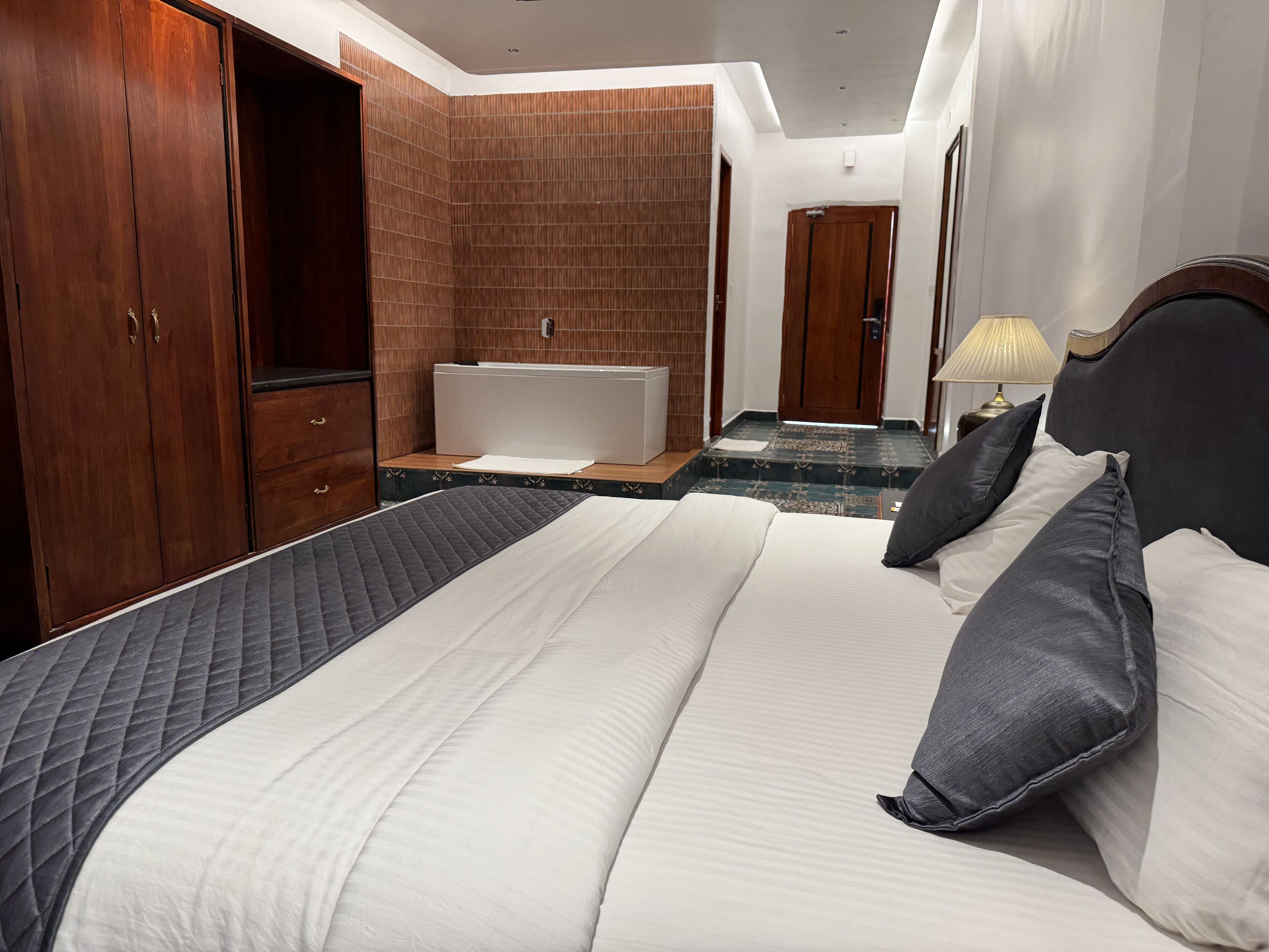 Habitación de hotel con una cama grande, un armario de madera, una bañera y un baño con espejo y toallero.