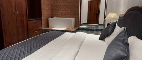 Habitación de hotel con una cama grande, un armario de madera, una bañera y un baño con espejo y toallero.