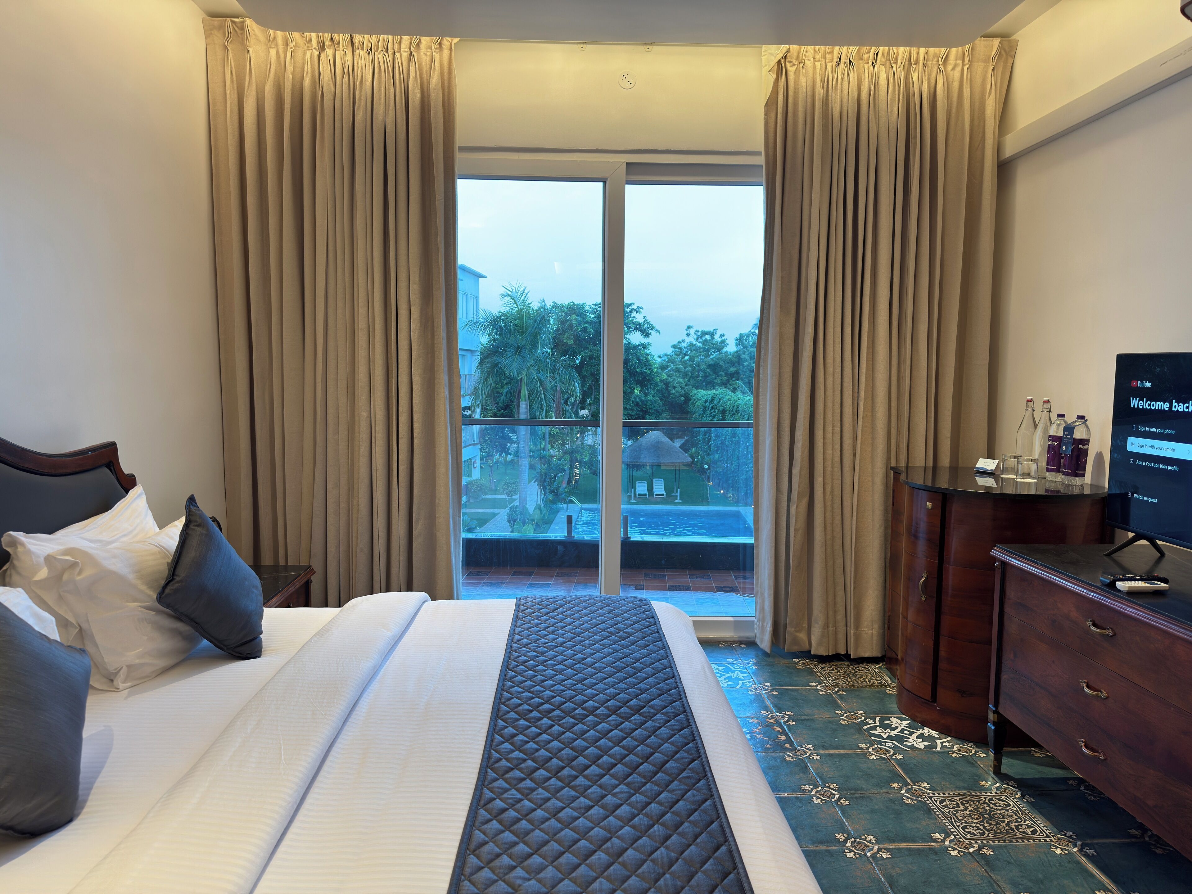 A hotel room with a bed, a TV, a dresser, and a balcony with a pool view.