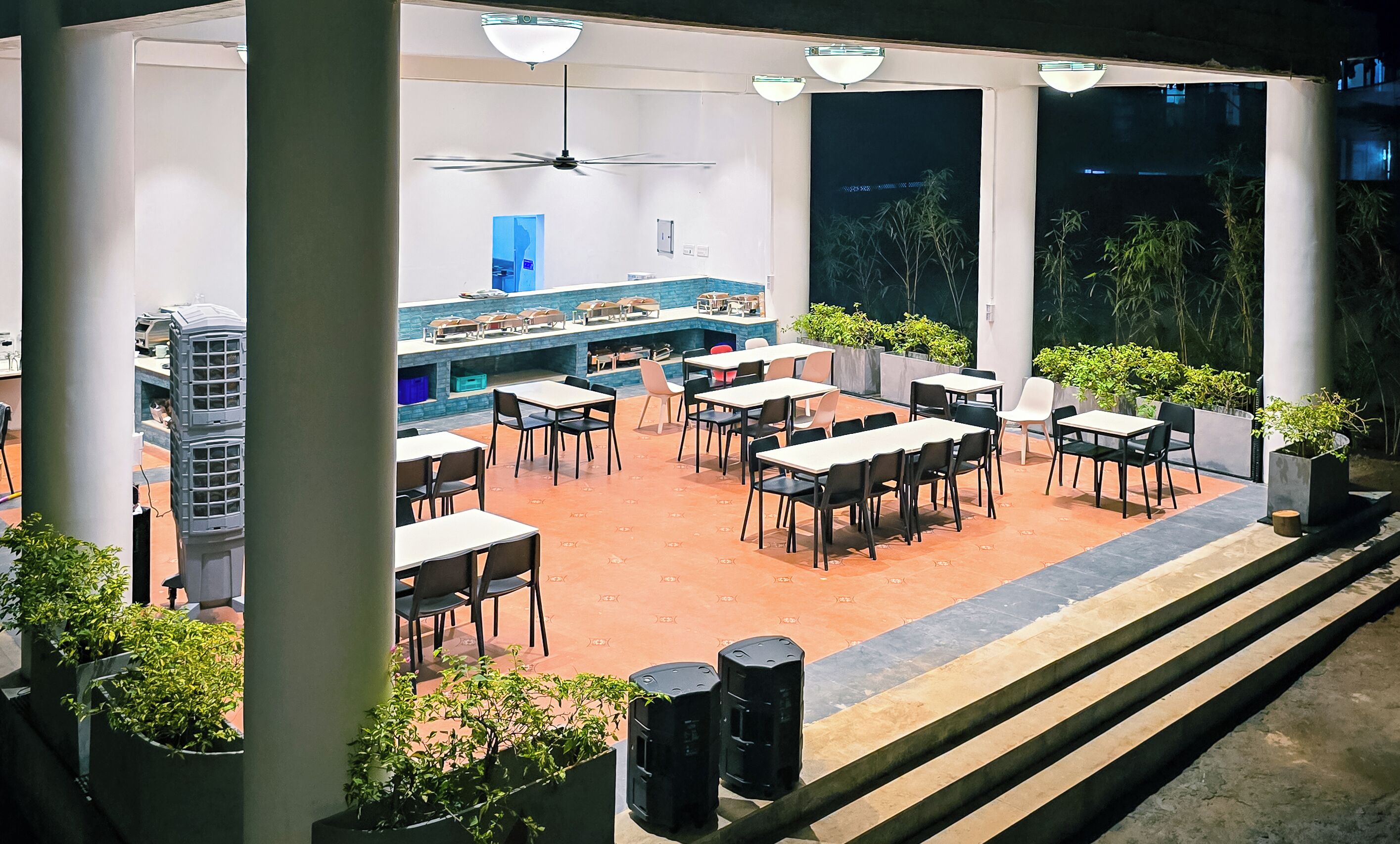 An outdoor dining area with tables and chairs, a counter with food display, and potted plants.