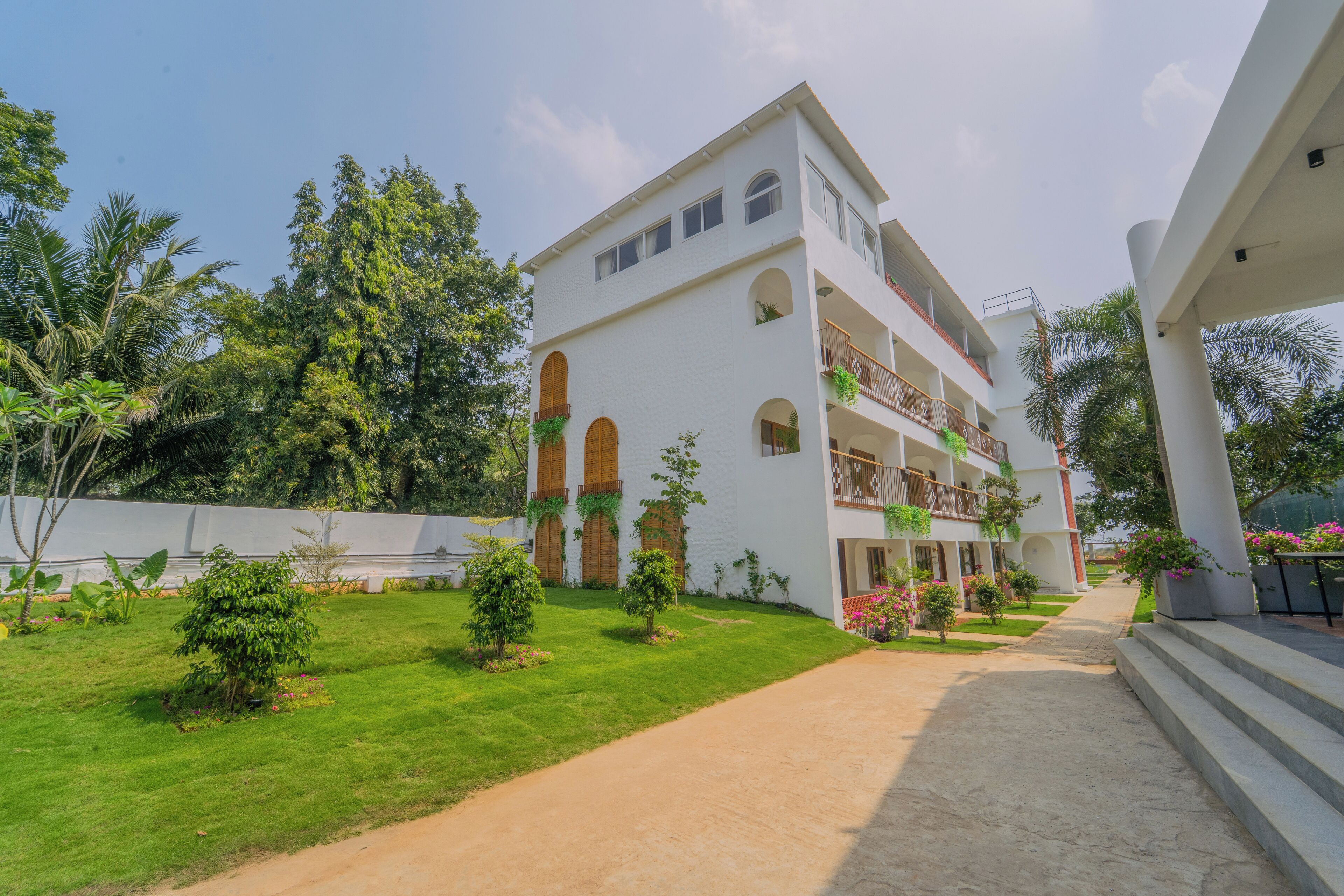 A multi-story building with a white facade, multiple balconies, and a well-maintained lawn.