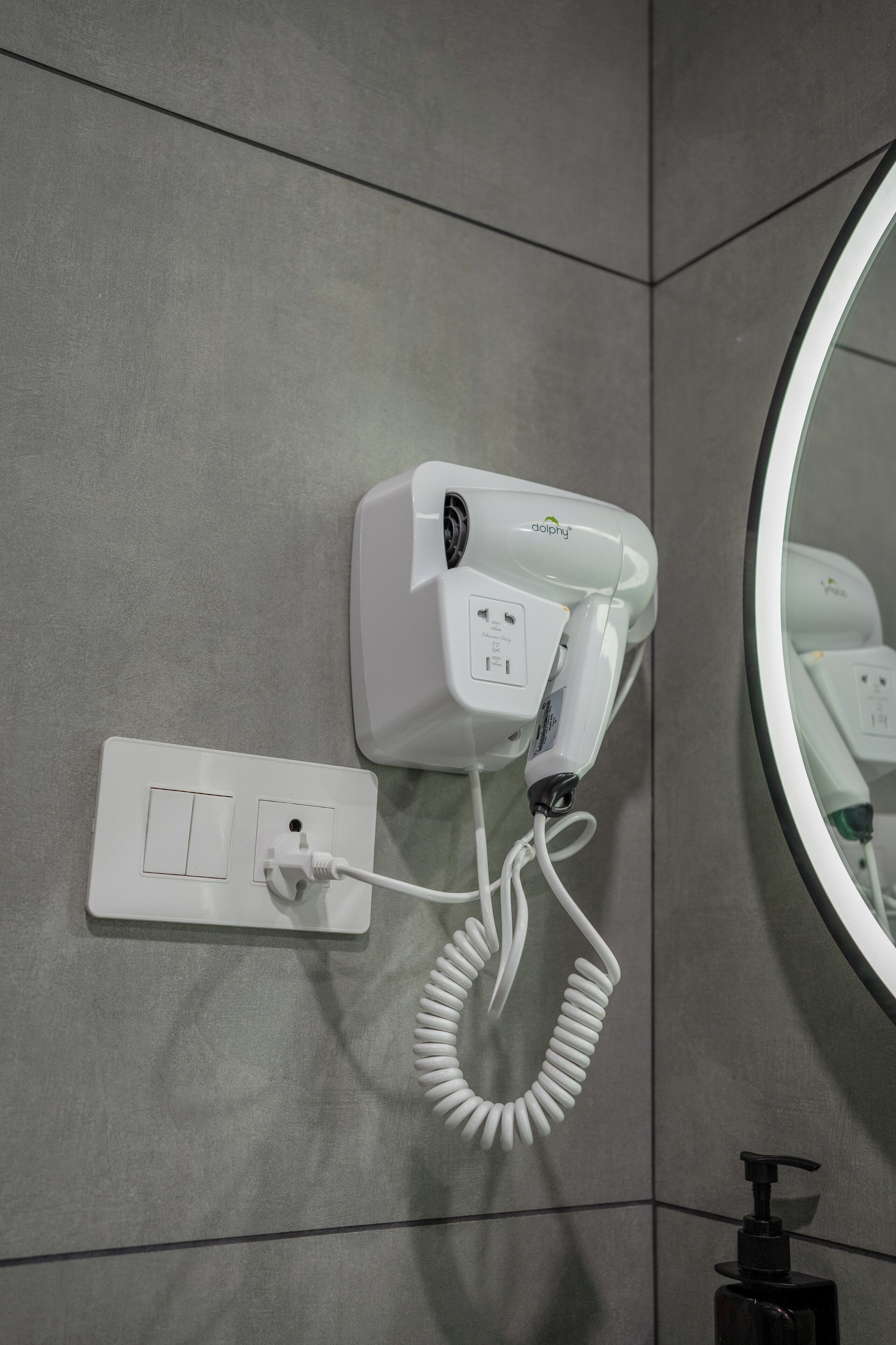 A hairdryer mounted on a wall with a power outlet and a mirror.