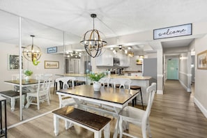 A modern kitchen with white cabinetry, a central island, and a dining area with white chairs and a wooden table.