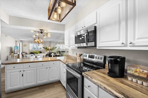 A modern kitchen with white cabinetry, a central island, a built-in oven, a microwave, and a coffee maker.