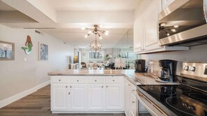 Una cocina moderna con armarios blancos, una isla grande, electrodomésticos de acero inoxidable y una araña.
