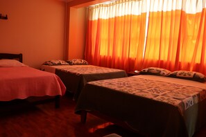 A hotel room with two single beds, each with a patterned bedspread and pillows. The room has wooden flooring and a window with orange curtains. - Hotel Virrey (San Ramón)