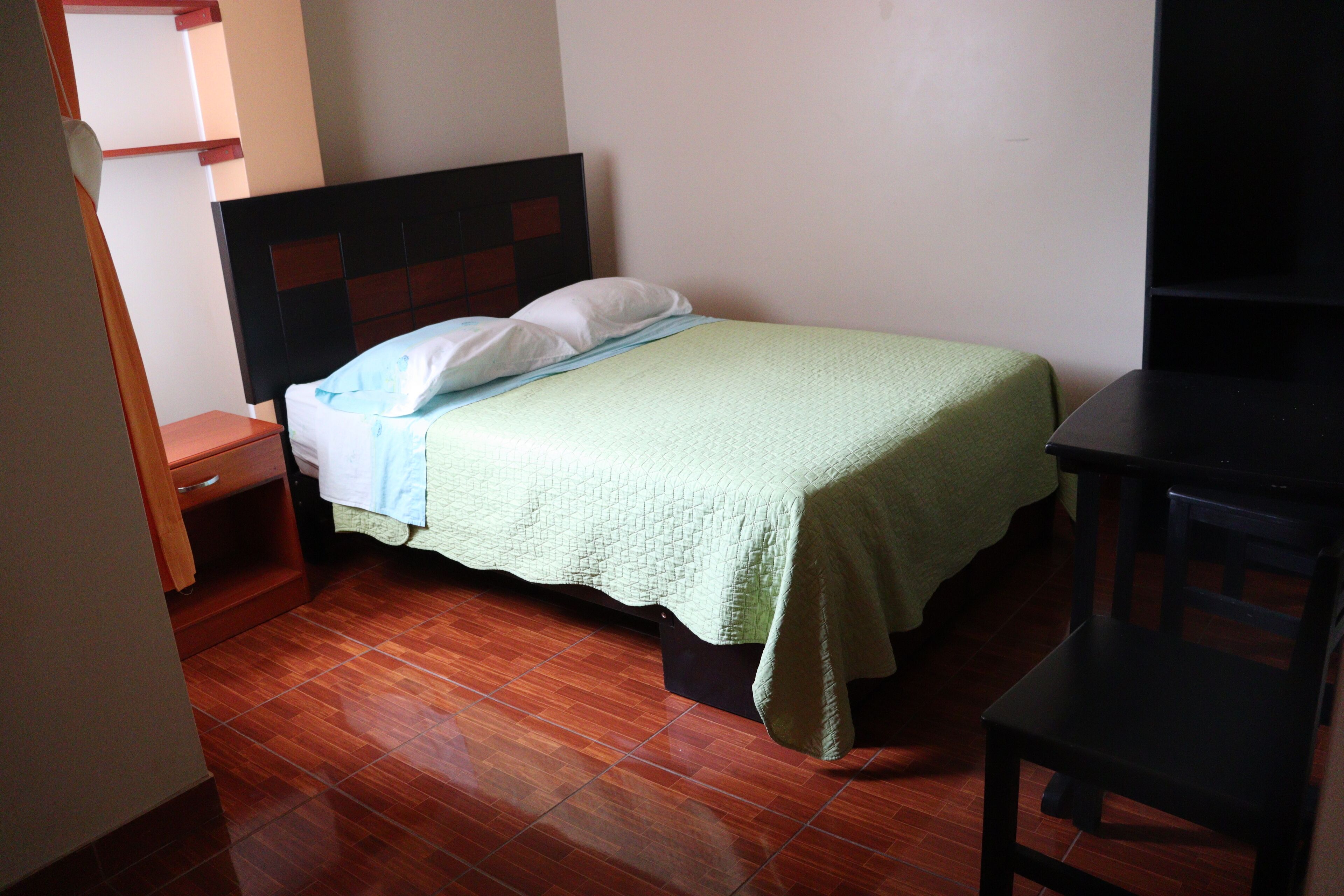 Una cama individual con cabecera de madera, una mesita de noche y un escritorio con una silla.