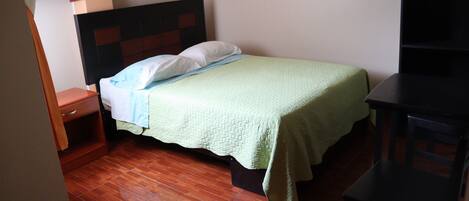 A single bed with a wooden headboard, a nightstand, and a desk with a chair.