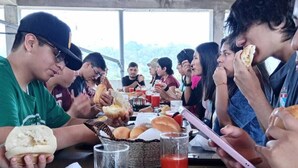 A group of people dining at a wooden table with plates of food, glasses, and a basket of bread. - Hotel Virrey (San Ramón)