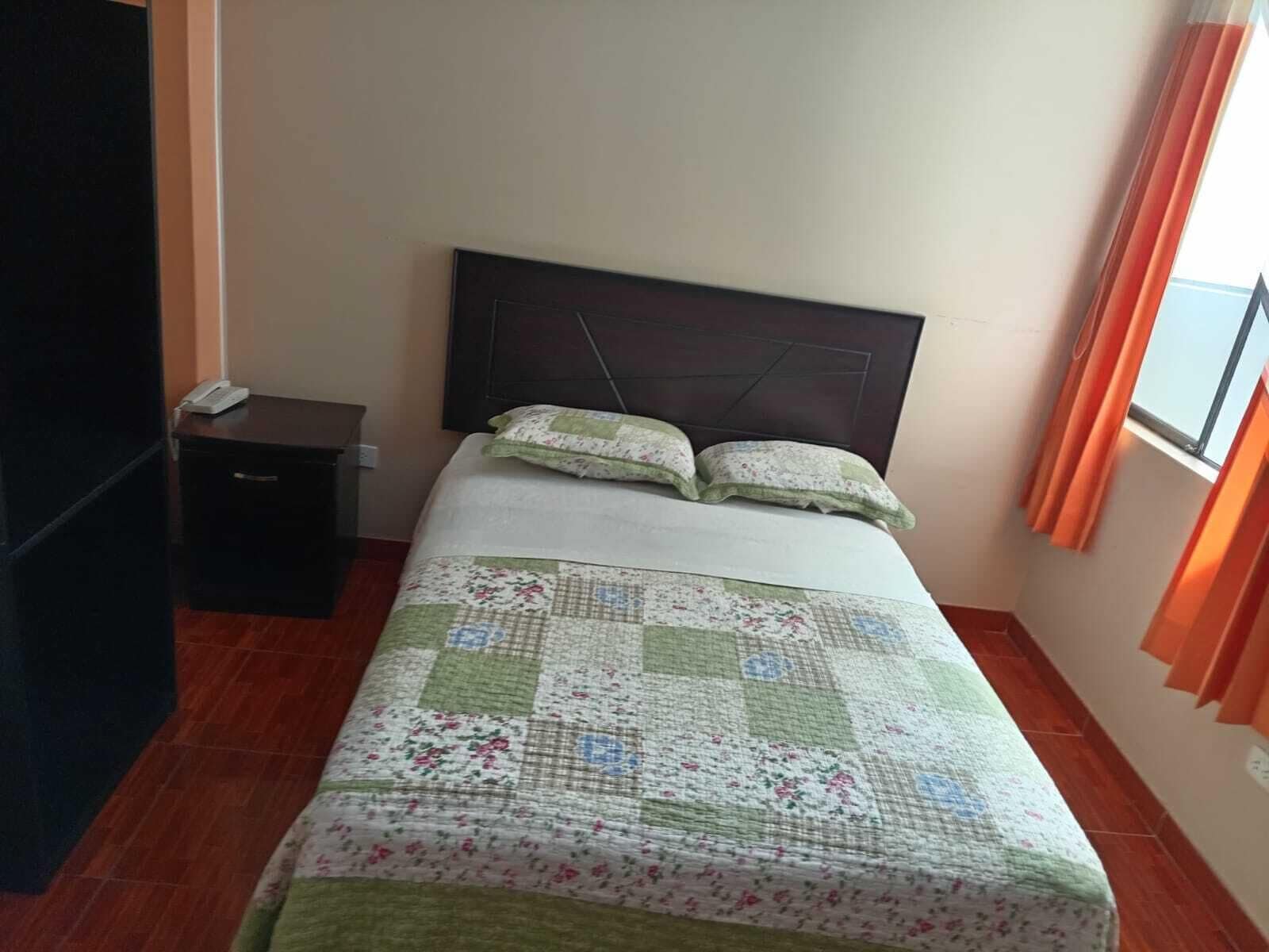 A bedroom with a bed, a nightstand, a dresser, and a window with curtains.