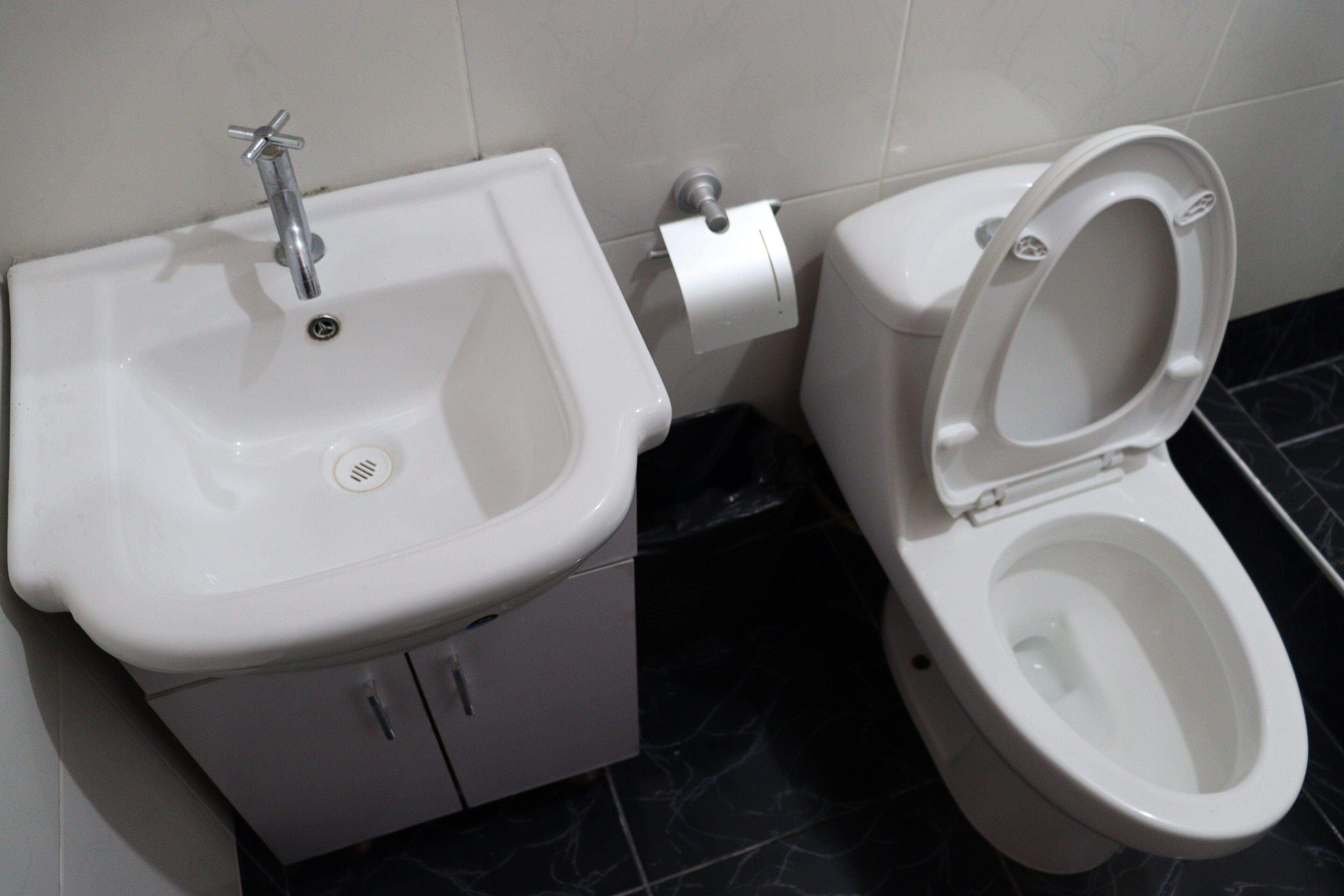 Un baño con lavamanos blanco, inodoro y piso de baldosas de mármol.