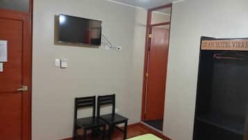 A hotel room with a bed, a television mounted on the wall, two chairs, and a door labeled "GRAN HOTEL VIRRE".