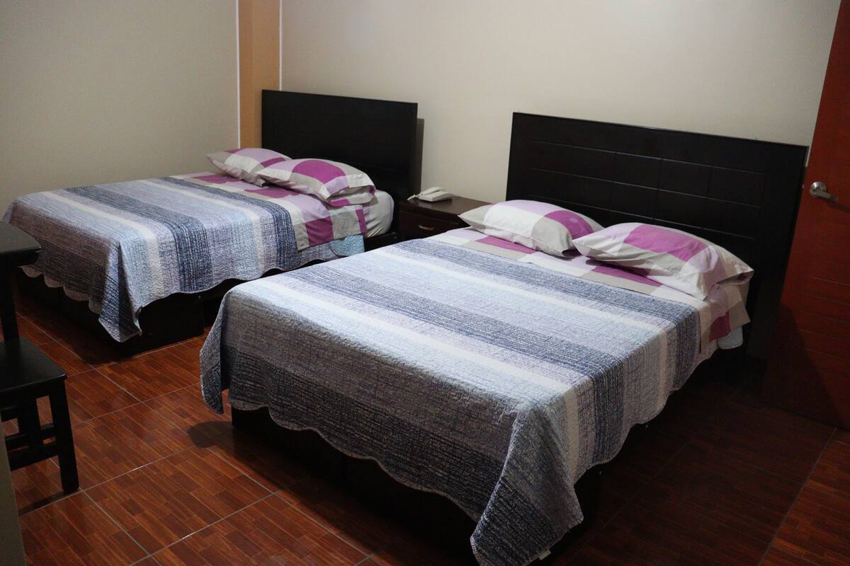 Two single beds with striped bedding, a wooden floor, and a nightstand with a phone.