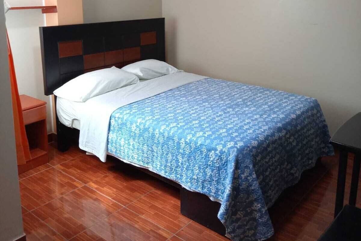 A single bed with a patterned bedspread, a nightstand, and a chair in a room with wooden flooring and a sloped ceiling.