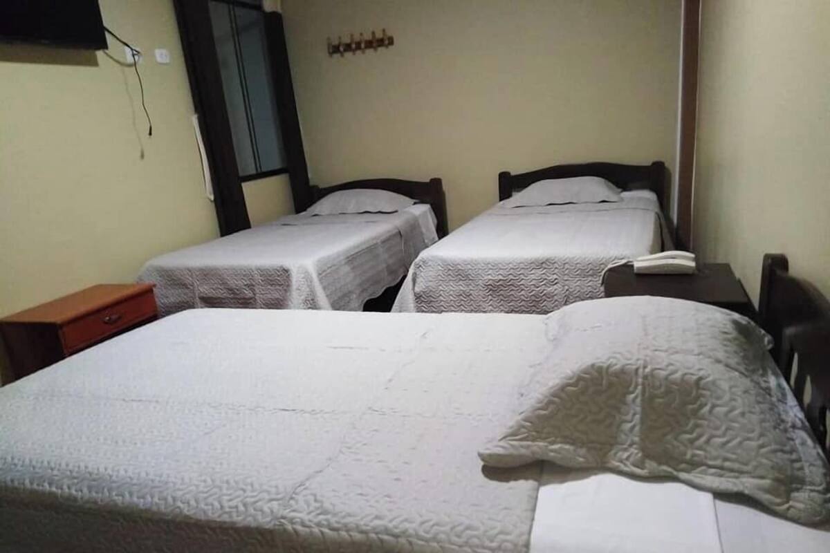 A hotel room with two single beds, a wooden nightstand, a small table, and a mirror on the wall.