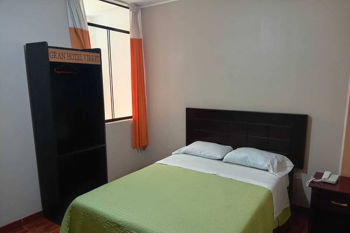 A hotel room with a bed, a nightstand, a wardrobe, and a window with curtains.