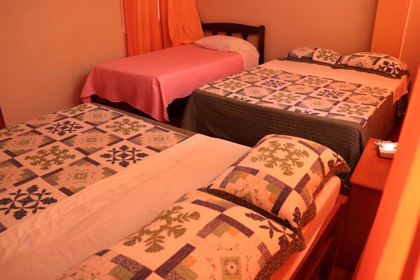 A room with three beds, each with a distinct quilt pattern.