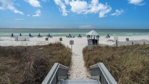Un sentier menant à une plage de sable, où l’on trouve des chaises longues et des parasols.