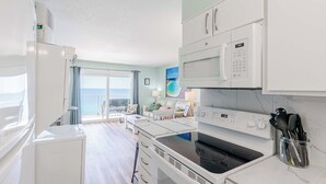 A modern kitchen with white appliances, a dining area, and a view of the sea. - Once Upon A Dream | Beachfront, Pools | Activity Passes (Panama City Beach)