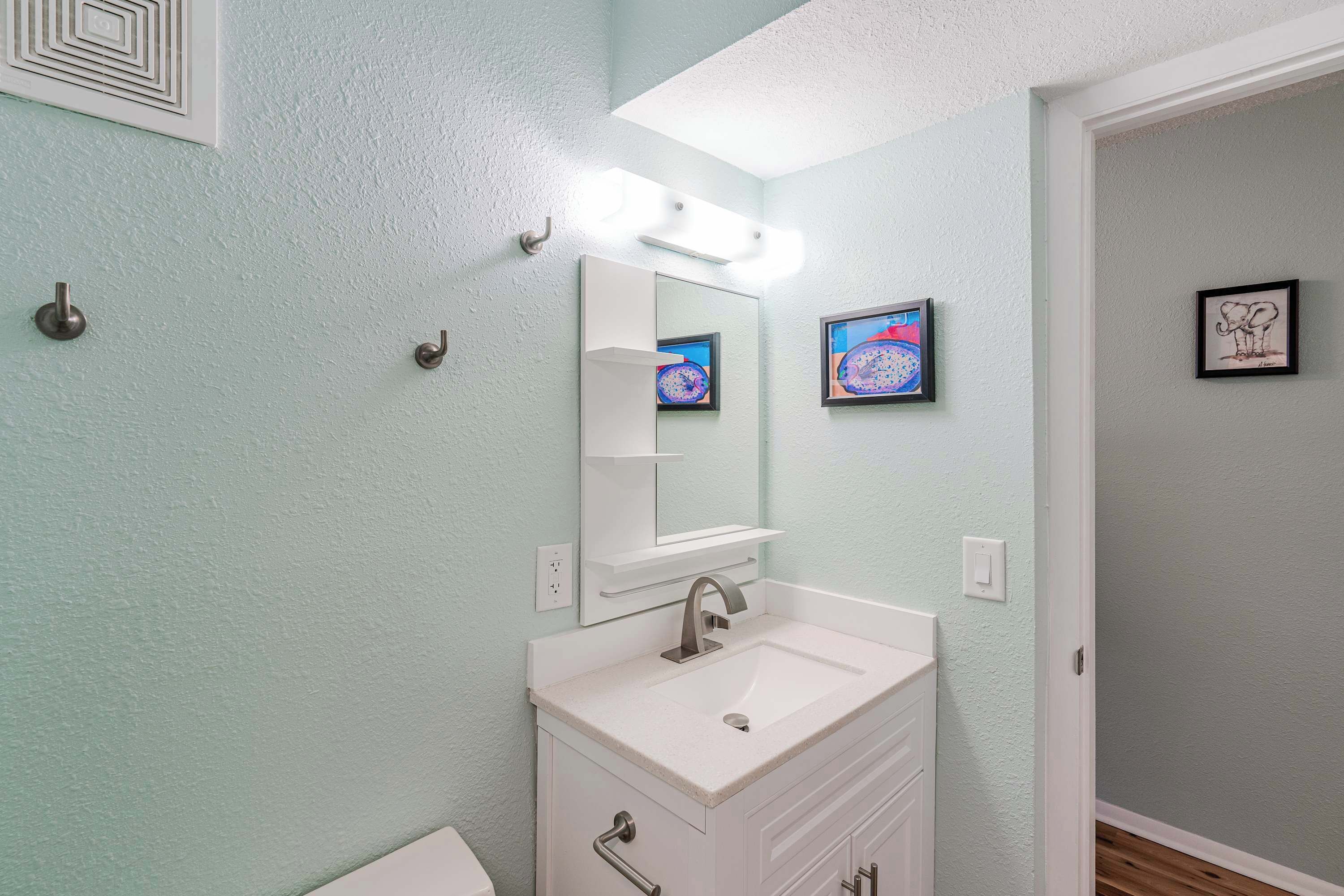A bathroom with a white vanity, a mirror, and a light fixture above the mirror.