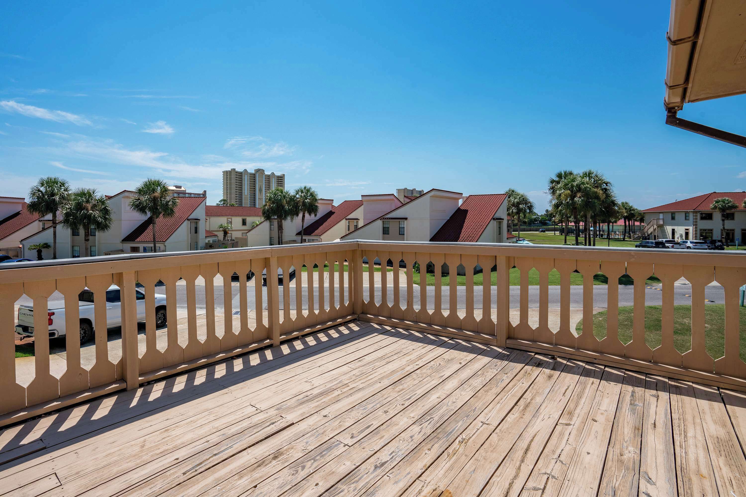 A wooden deck with a decorative railing, overlooking a row of buildings with red roofs and palm trees.