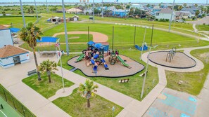 Ein Spielplatz mit Rutschen und Klettergerüsten, umgeben von einem gepflegten Rasen und einem Baseballfeld.