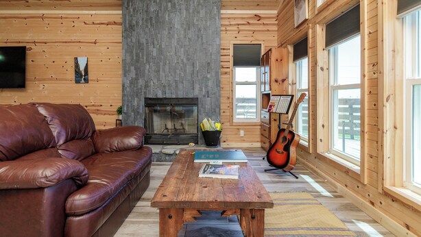 Un salon chaleureux avec un canapé en cuir, une table basse en bois, une cheminée et une grande fenêtre donnant sur un beau paysage.