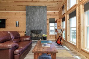 Un salon chaleureux avec un canapé en cuir, une table basse en bois, une cheminée et une grande fenêtre donnant sur un beau paysage.