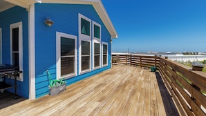 Un bâtiment bleu doté d’une terrasse en bois, de grandes fenêtres et offrant une vue sur l’océan.