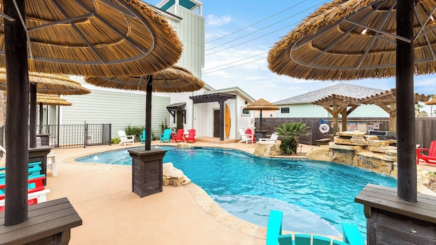 Ein Pool mit Strohdächern, bunten Stühlen und einer Wasserfallanlage aus Stein.
