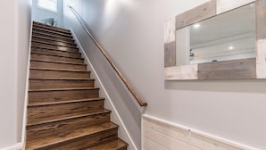 Eine Holztreppe mit Geländer, weißen Wänden und einem spiegelnden Wandbild mit Holzrahmen.