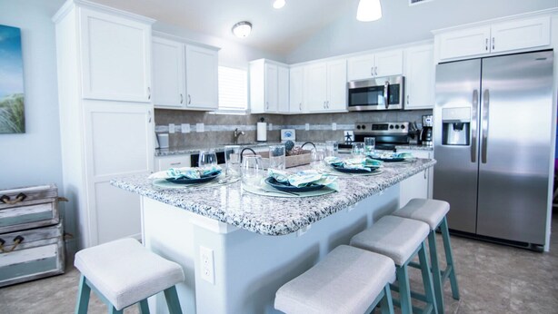 A modern kitchen with white cabinets, a granite countertop, stainless steel appliances, and bar stools. - Off da Hook Private Heated Pool | Pet Friendly (Port Aransas)