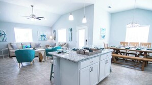 A spacious kitchen with a central island, a dining area with wooden tables, and a living area with a sofa and chairs. - Off da Hook Private Heated Pool | Pet Friendly (Port Aransas)