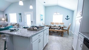 A kitchen with a granite countertop, wooden dining table, and white cabinets. - Off da Hook Private Heated Pool | Pet Friendly (Port Aransas)